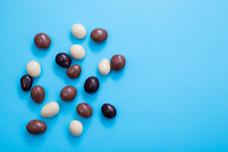 close up of chocolate egg and candy drops on blue background