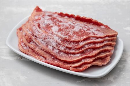 frozen meat on white dish on ceramic background