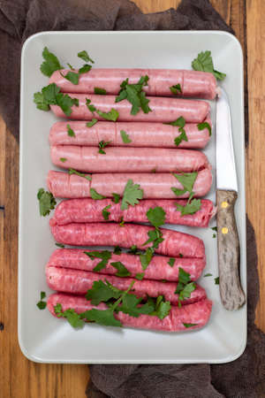 raw fresh sausages on gray dish on wooden background