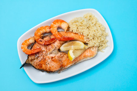 fried salmon with shrimps and cous-cous on white dish on blue backgroundの写真素材