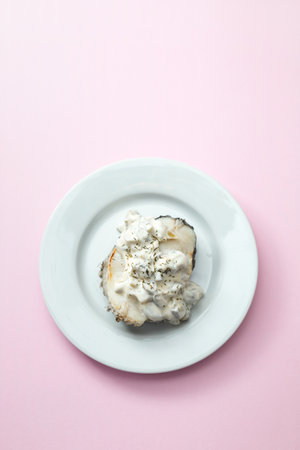 boiled fish with sauce on white plate on pink background