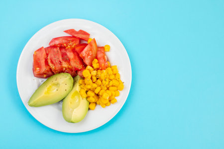 corn, tomato and avocado salad on white plate on blue backgroundの写真素材