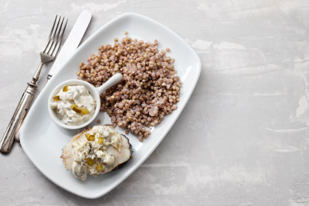 boiled fish with buckwheat and sauce on white dish on ceramic backgroundの写真素材