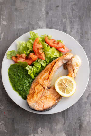 fried salmon with spinach and salad on white plateの写真素材