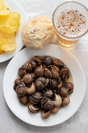 boiled snails with bear, bread, olives and potato chips on ceramic backgroundの写真素材