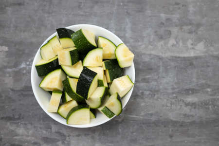 fresh courgette in cubes in small white bowl on ceramic backgroundの写真素材