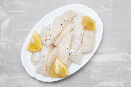 raw squid with pepper and fresh lemon on white dish on ceramic backgroundの写真素材