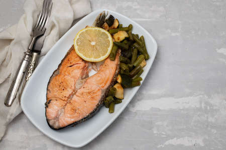 fried salmon with fresh lemon and spinach on white dish on ceramic backgroundの写真素材