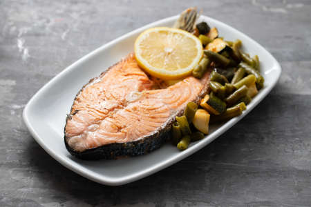 fried salmon with fresh lemon and spinach on white dish on ceramic backgroundの写真素材
