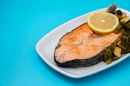 fried salmon with fresh lemon and spinach on white dish on blue paperの写真素材
