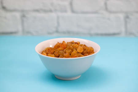dry yellow grapes in small white bowl on blue paperの写真素材