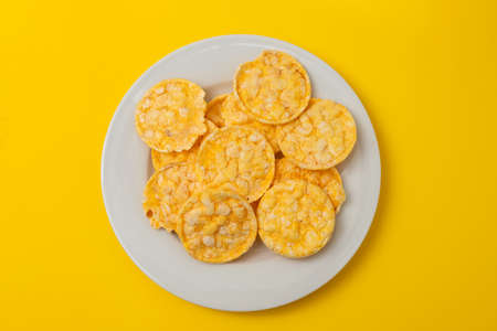 small puffed corn cakes on small white plate on yellow paperの写真素材