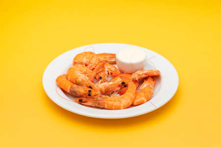 Boiled fresh whole shrimps with sauce in small bowl on white plate on yellow paperの写真素材