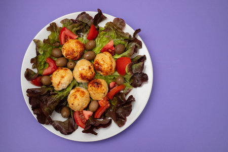 Chicken meatballs on lettuce with tomato and olives on white dishの写真素材