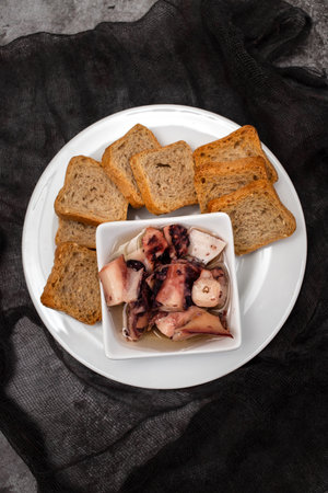 octopus salad with oil in small bowl and toasts on white plateの写真素材
