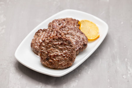 grilled meat cutlets for burger with lemon on big white dishの写真素材