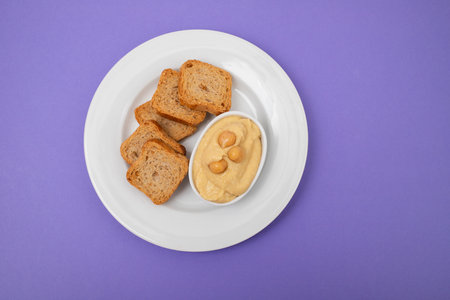 a bowl of hummus dip with mini toasts on white plate