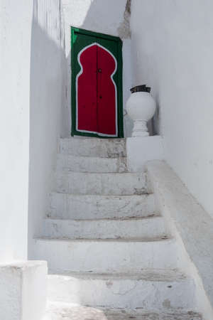 A white, stone staircase leading to a red door. Maghreb style. Tunisia. Sidi Bou Said.の写真素材