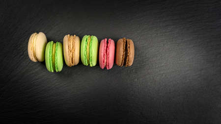 Multicolored macarons in a row on a black background with copy spaceの写真素材