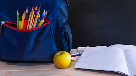 School concept backpack on desk with school accessories and copy space on chalk board, back to...