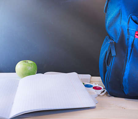 School concept, blue backpack with pencils on the table in front of the chalk board stands on the table with notebooks, apples, paints, extra wide banner with copy spaceの写真素材