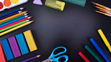Everything for creativity, various stationery on a black background of a chalk board with copy space: scissors, felt-tip pens, plasticine, pens, pencils, ruler, eraser, sharpenerの写真素材