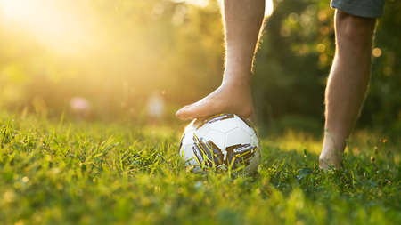 Male foot without shoes on a soccer ball on a grassy field with a sun glare and a copy space.の写真素材