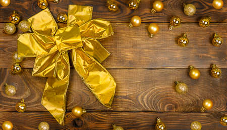 Big golden bow and golden Christmas balls on a dark brown wooden table background with copy space, top view