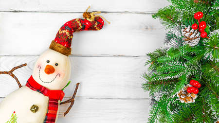 Christmas toy snowman and spruce branches on white wooden background with copy space, front view for postcards and gift bagsの写真素材