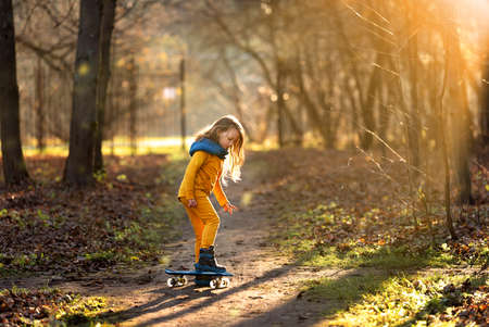 Teenage girl riding a skateboard in a city park in autumn, photo with beautiful lightの写真素材