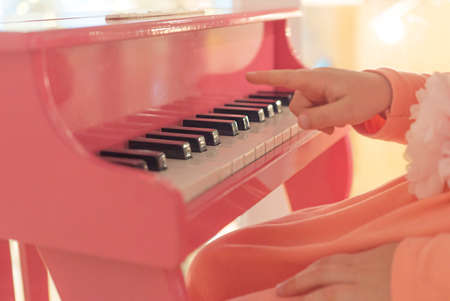 Child girl playing on pink childrens piano, close-up photoの写真素材