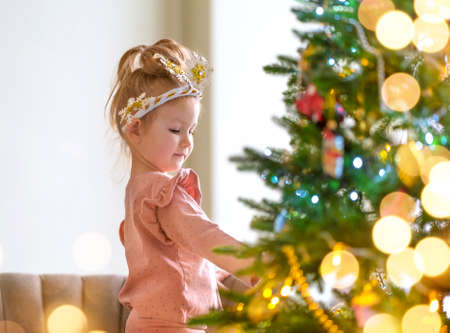 Little girl in pajamas decorates christmas tree at homeの写真素材