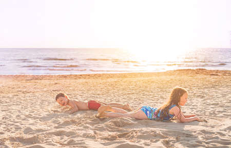 Children on the beach near the sea play with sand in the summer at sunsetの写真素材