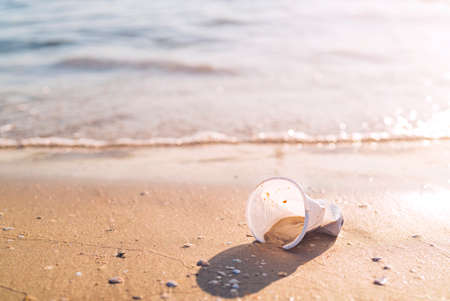 A plastic cup lying on the beach by the oceanの写真素材