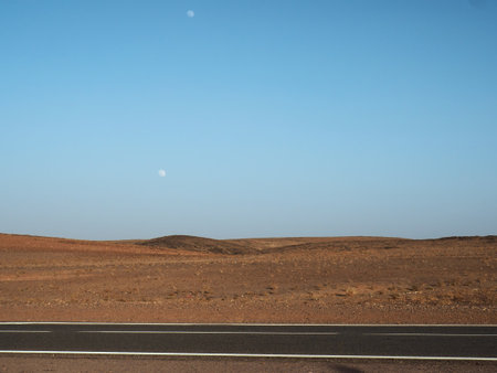 Desert asphalt route and Moon over desert landscape at early evening.の写真素材