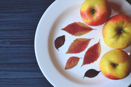 Apples in a white plate on a wooden table. Ripened apples. Autumn leaves decor.の写真素材