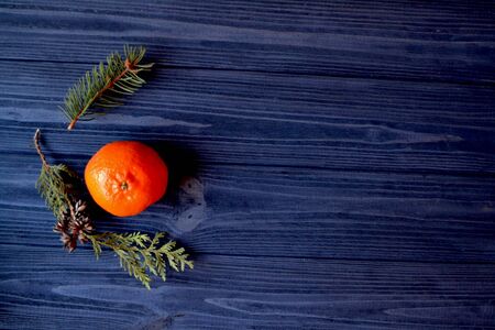 Flat lay background with branches of fir-tree and tangerine. Orange mandarine and green branches of fir-tree on the dark blue wooden table. Background with place for text.の写真素材
