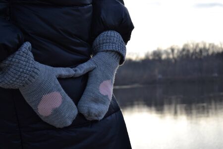 Girl's hands in mittens with love hearts near the lake.の写真素材