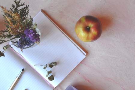 Vintage backgound for greeting card. Beautful flat lay. Apple, bouquet in vase, opened notebook on the pink concrete table.の写真素材