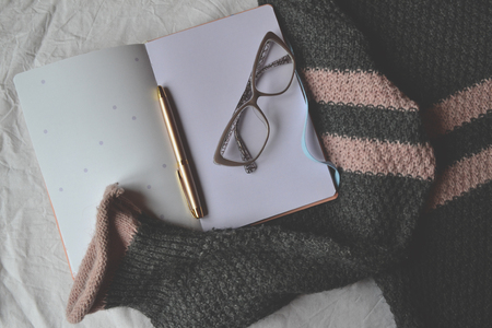 Opened notebook, pen, glasses and sweater on the bed. Woman's accessories.の写真素材