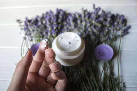 Lavender flowers, candles, cream and female hand on a white wooden background. Beauty care. Top view.の写真素材