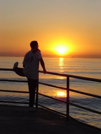            young men streatching, sunset, huntington beach, california