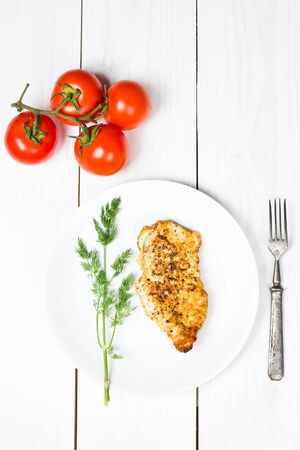 Grilled tasty chicken breasts on a white plate with fresh tomatoes and herbs on wooden backgroundの写真素材