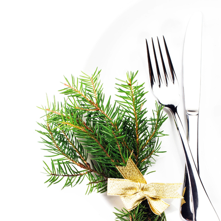 Christmas table setting with festive decorations on white plate isolated on white background. Christmas tree branch, golden stars, Fork and knife with copy space, macro.の写真素材