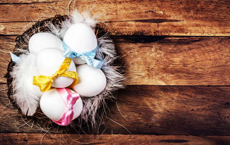 Easter nest with Eggs,  ribbons and white feathers on wooden background with copy space for text in...