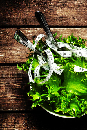 Salad in a bowl with  measuring tape over wooden table with knife and fork.  Diet Food and healthy lifestyle concept.の写真素材