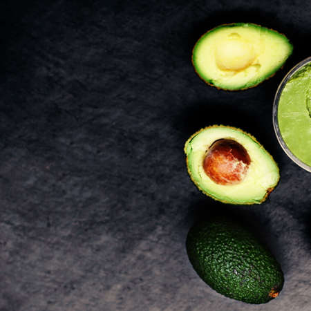 Halved and whole ripe avocados over black background. Top view.の写真素材