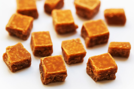 Salted caramel pieces and sea salt close up over white background.