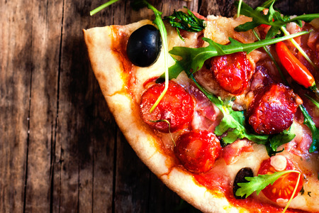 Hot pizza slice with Pepperoni, melting cheese on a rustic wooden table close up.の写真素材