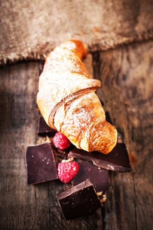 Fresh delicious croissant with chocolate  and raspberries on old wooden background close up
の写真素材